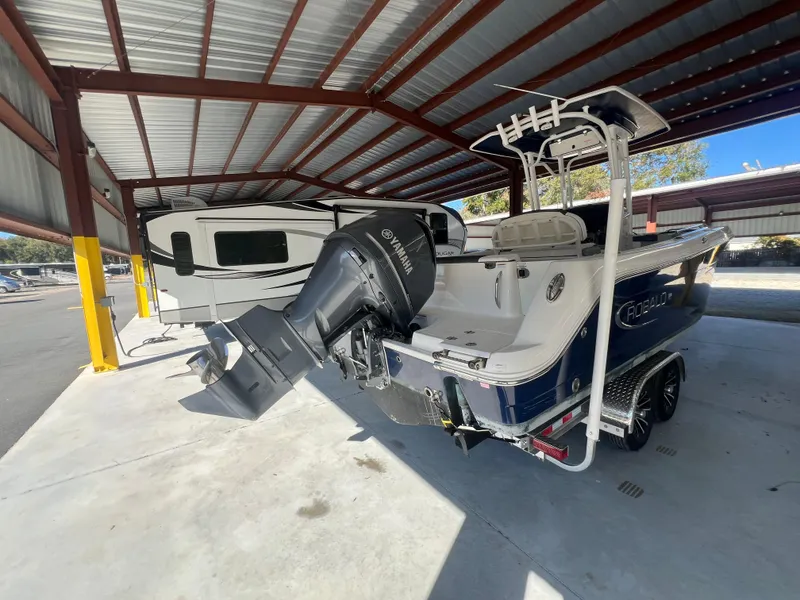 Slide: The Image of 2019 Robalo R242 Explorer boat under a metal canopy, parked beside a trailer. - 3