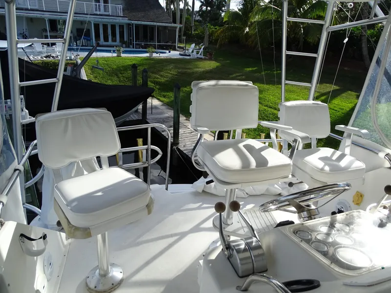 Slide: The Image of Ocean Yachts 48 cockpit, 1987 model, featuring white seating and controls, docked near a house. - 32