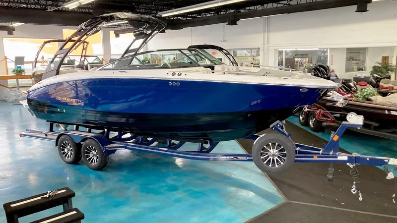 The Image of 2025 Regal LS6 Surf boat in showroom, blue hull, on trailer. - 0