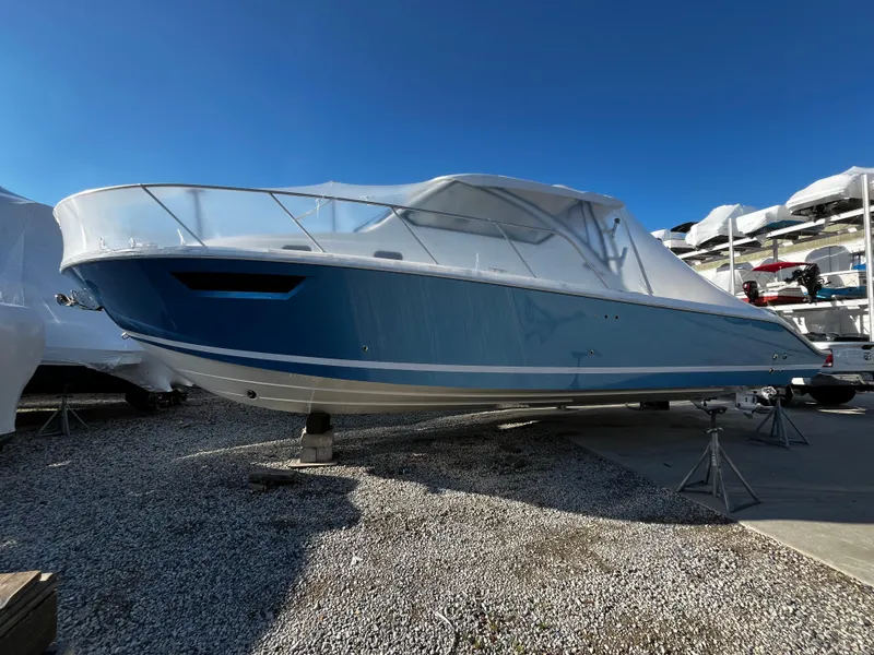 Slide: The Image of 2024 Pursuit OS 325 boat on display, blue hull, covered, outdoor setting. - 0