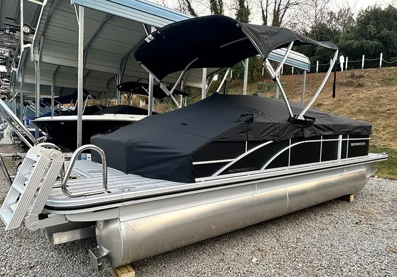 Slide: The Image of 2025 Bennington SX 22 Swingback pontoon boat with black cover, parked on gravel. - 0