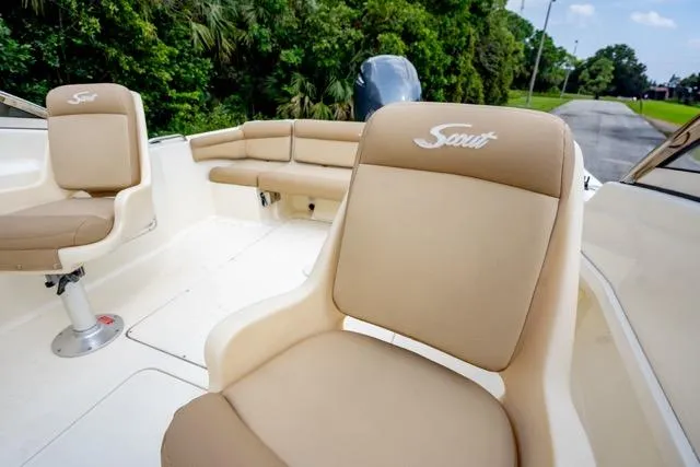 Slide: The Image of 2021 Scout 210 Dorado boat interior with beige seating and lush greenery background. - 12