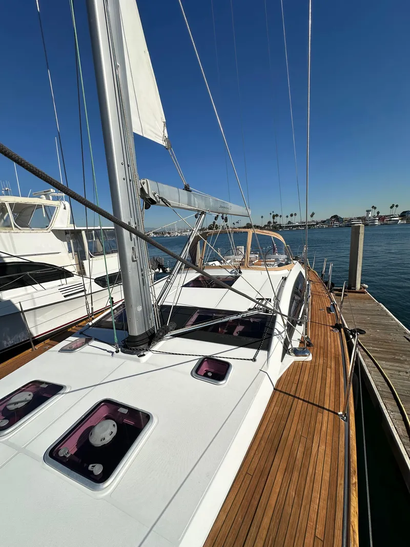 Slide: The Image of 2013 Jeanneau 57 yacht docked, showcasing sleek deck and mast under clear blue sky. - 25