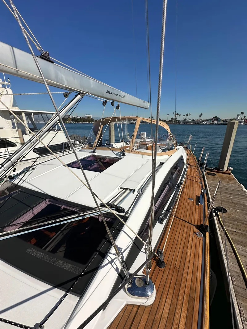 Slide: The Image of 2013 Jeanneau 57 yacht docked, showcasing sleek design and wooden deck. - 26