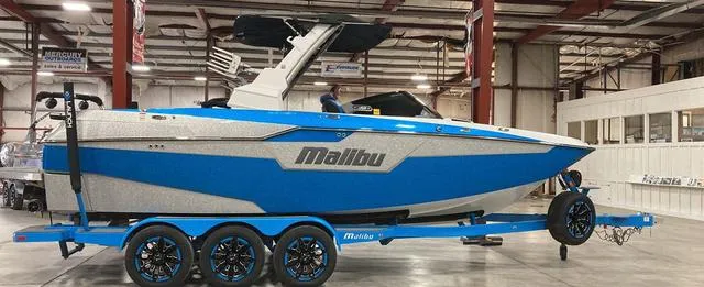 Slide: The Image of 2021 Malibu M240 boat in a showroom, blue and white design on a trailer. - 1