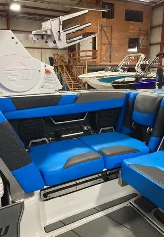 Slide: The Image of 2021 Malibu M240 boat interior with blue and black seating in a warehouse setting. - 10