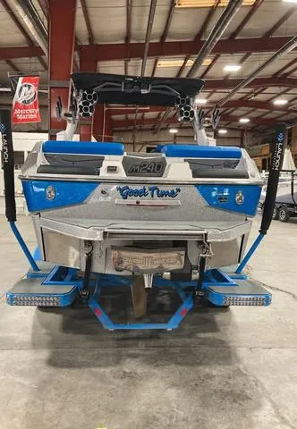 Slide: The Image of 2021 Malibu M240 boat in warehouse, rear view, blue and silver design. - 2