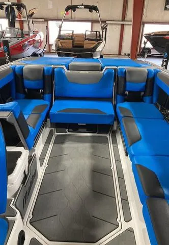 Slide: The Image of 2021 Malibu M240 boat interior with blue and black seating in a showroom. - 6