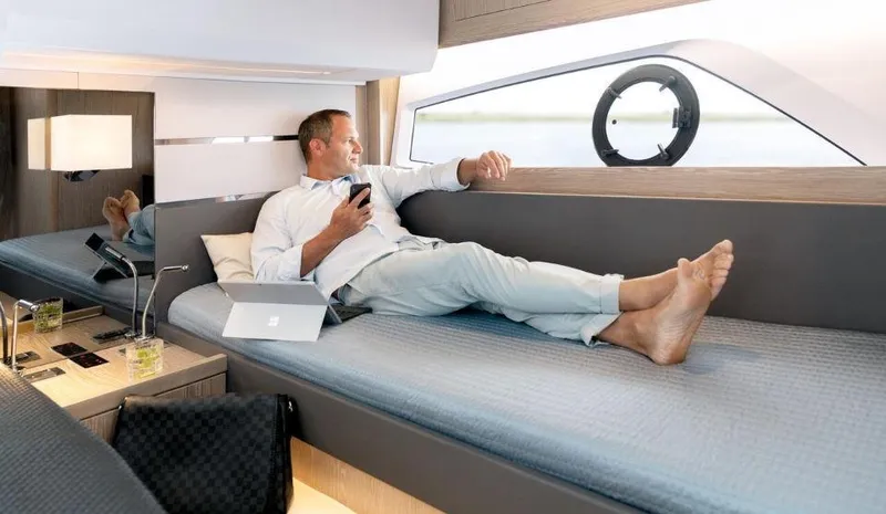 Slide: The Image of Man relaxing on a 2025 Sealine F430 yacht interior, holding a phone. - 38