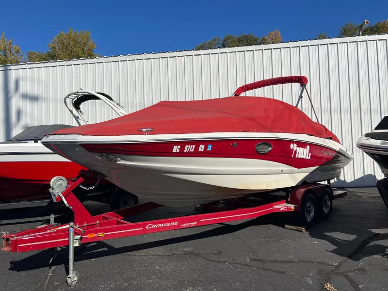 Slide: The Image of 2013 Crownline Q4 boat with red cover on trailer, parked outdoors. - 2