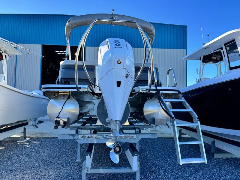 Slide: The Image of 2025 Bennington 24 MFB boat with outboard motor on trailer, docked between two boats. - 5