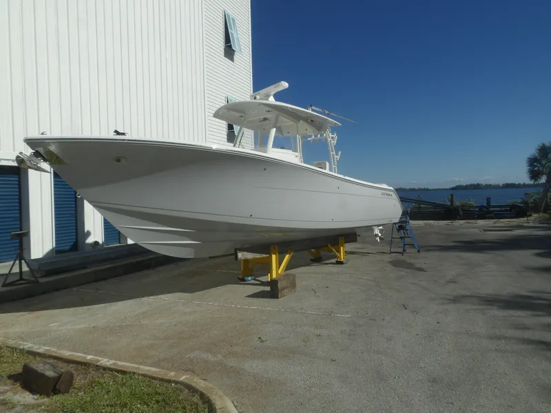 The Image of 2020 Cobia 320 Center Console boat on stands near waterfront building. - 0