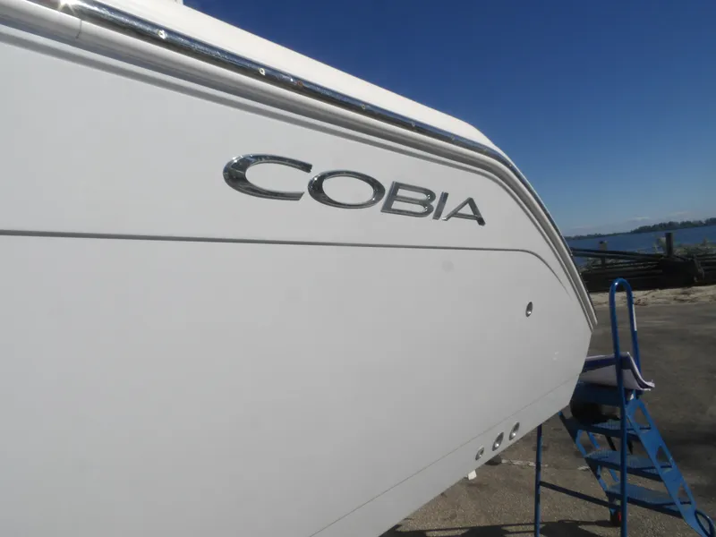 Slide: The Image of 2020 Cobia 320 Center Console boat side view with logo, docked near water. - 8