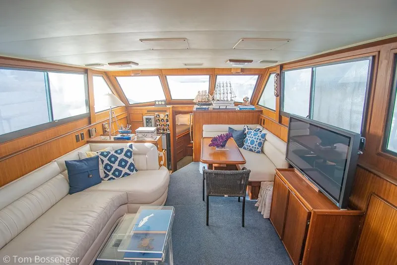Slide: The Image of 1986 Hatteras 43 Motor Yacht interior with cozy seating, wooden accents, and large windows. - 9
