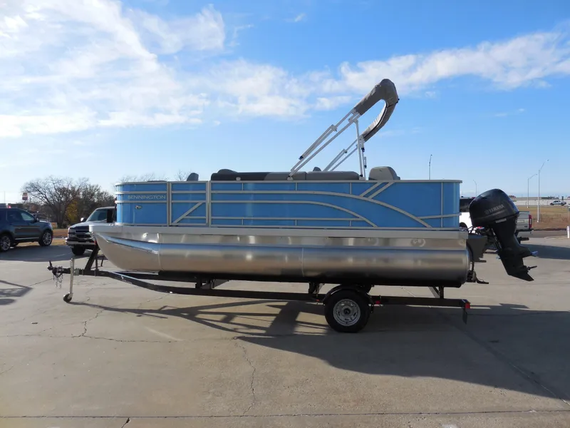 Slide: The Image of 2025 Bennington 188 SF pontoon boat on trailer, blue and silver design, parked outdoors. - 4
