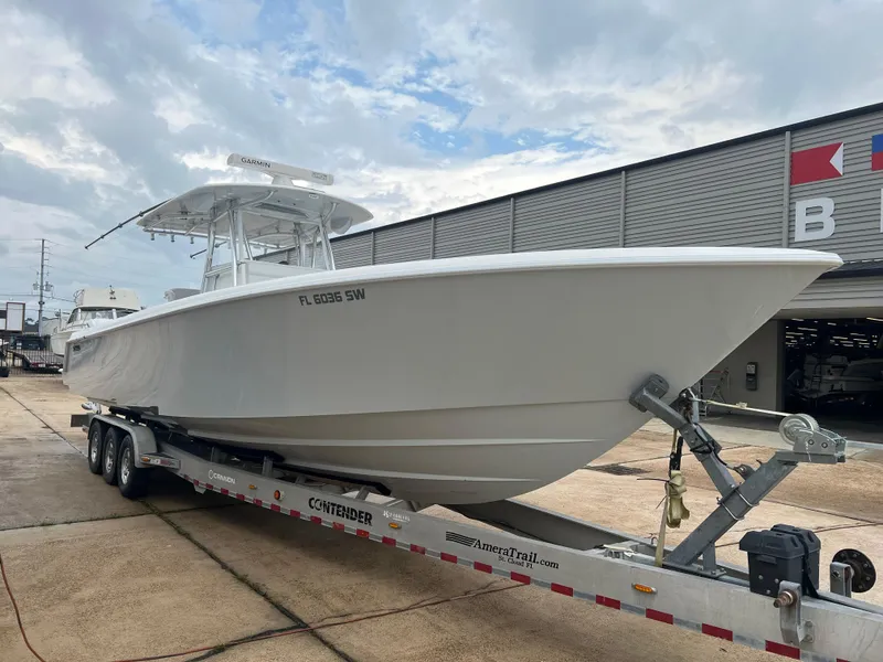 Slide: The Image of 2021 Contender 39 ST boat on trailer, parked outside a building under cloudy sky. - 2