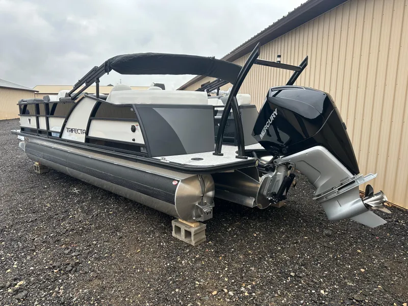 Slide: The Image of 2025 Trifecta 23 RFESS pontoon boat with Mercury outboard engine, parked on gravel. - 4