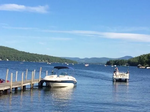 Slide: The Image of 2003 Sea Ray 240 Sundeck boat docked on a serene lake with scenic mountain views. - 12