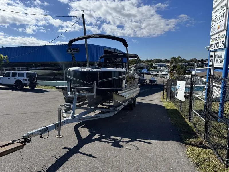 Slide: The Image of 2025 Avalon LSZ Quad Lounger boat on trailer at marina under blue sky. - 2