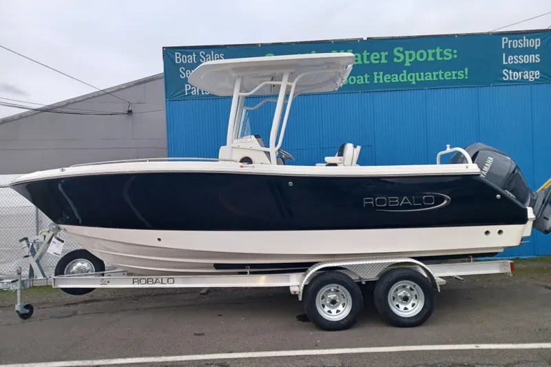 The Image of 2025 Robalo R230 Center Console boat on trailer, parked outside a marine store. - 0