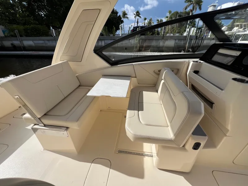 Slide: The Image of 2025 Scout 277 Dorado boat interior with beige seating and table, dockside view. - 21