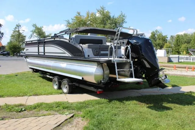Slide: The Image of 2024 Harris Solstice 250 SL pontoon boat on trailer, parked on grass. - 4