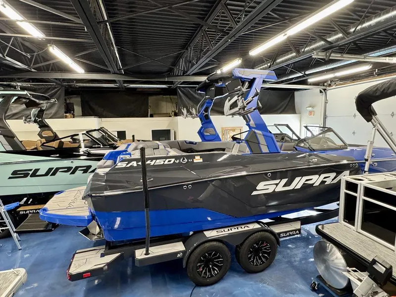 Slide: The Image of 2025 Supra SA 450 boat in showroom, blue and black design, on trailer. - 6