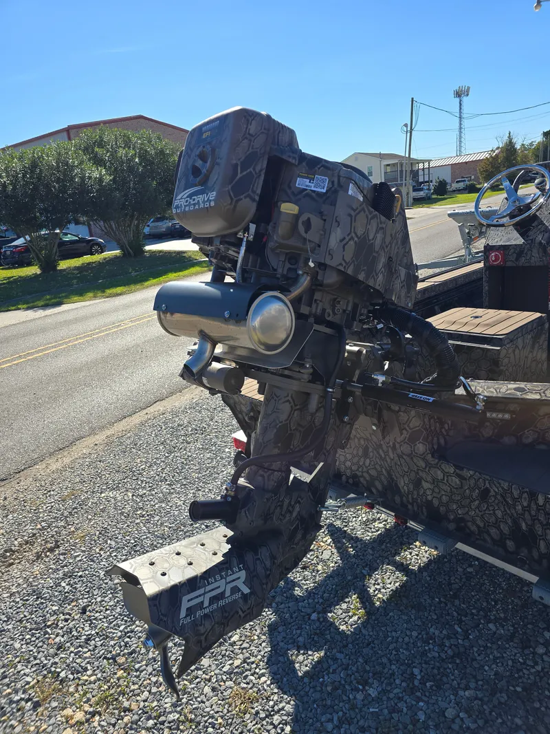 Slide: The Image of 2024 Pro-Drive X Series 1860 CC boat motor in camouflage design, parked on gravel. - 7
