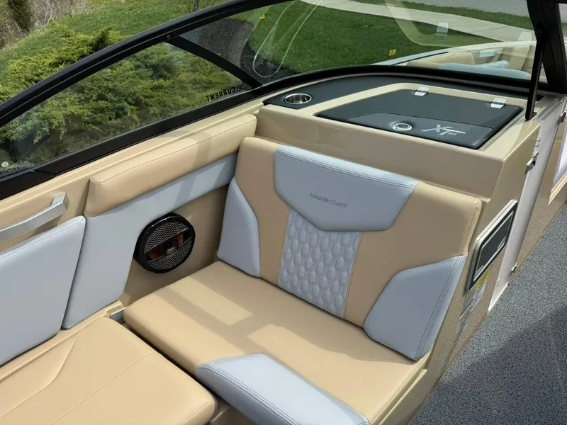 Slide: The Image of 2024 MasterCraft XT24 boat interior with beige and gray seating, featuring a speaker and storage area. - 11