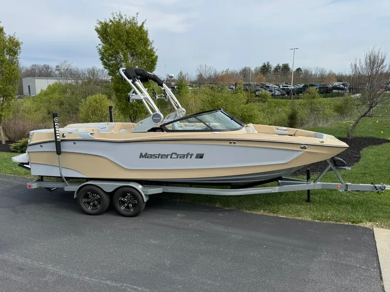 Slide: The Image of 2024 MasterCraft XT24 boat on trailer, parked outdoors, surrounded by greenery. - 14