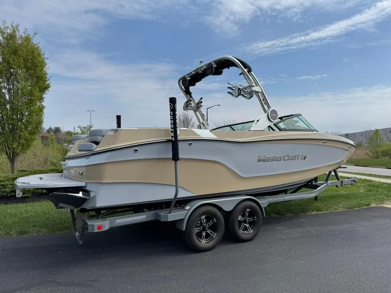 Slide: The Image of 2024 MasterCraft XT24 boat on trailer, parked outdoors under a partly cloudy sky. - 4