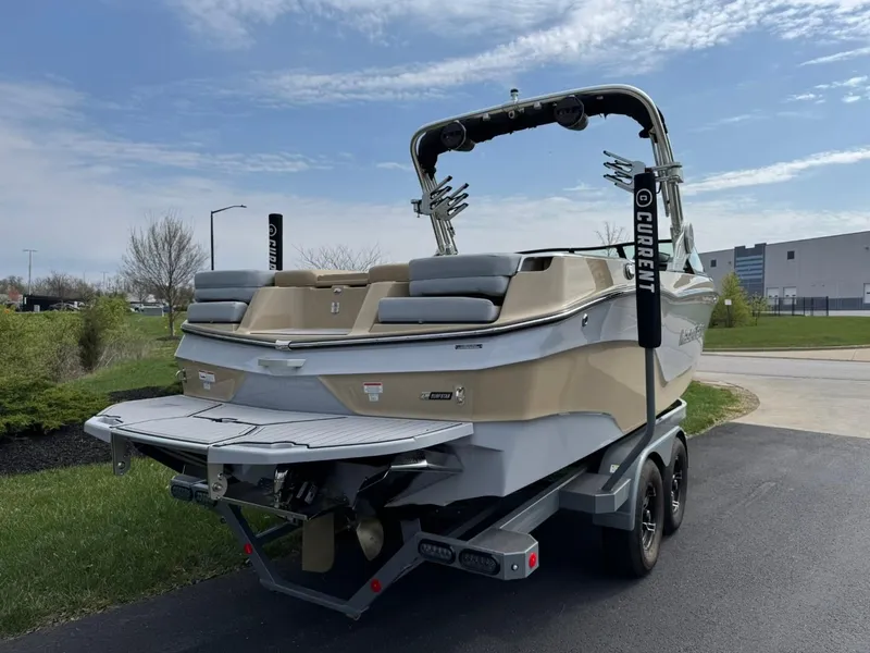 Slide: The Image of 2024 MasterCraft XT24 boat on trailer, parked outdoors under a partly cloudy sky. - 5