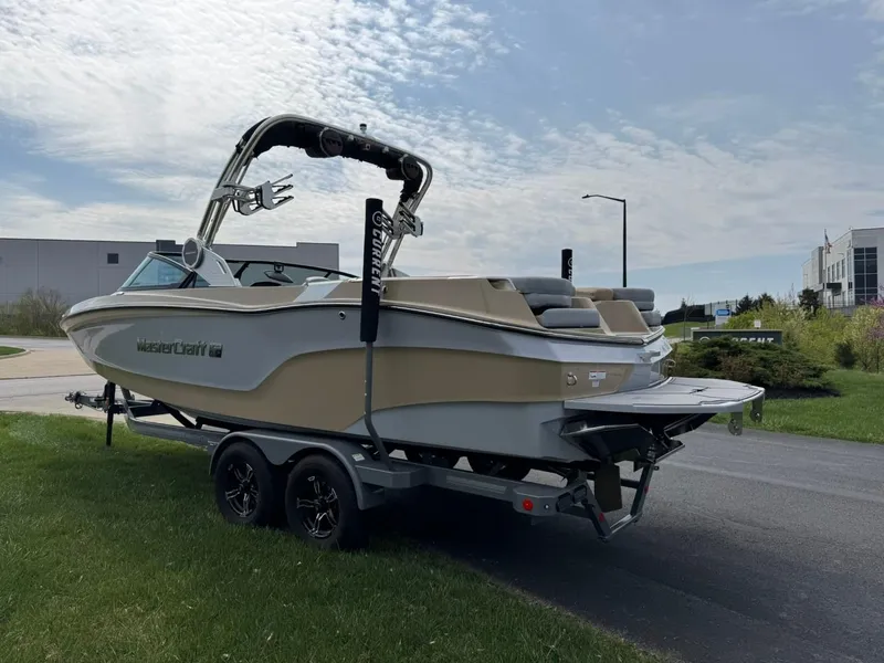 Slide: The Image of 2024 MasterCraft XT24 boat on trailer, parked on grass, under a partly cloudy sky. - 7