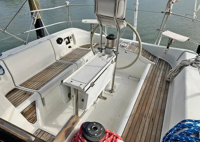 Slide: The Image of 1990 Beneteau Sloop cockpit with wooden deck and steering wheel, docked by the water. - 4