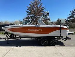 Slide: The Image of 2024 MasterCraft X22 boat on trailer, orange and white design, parked outdoors. - 6