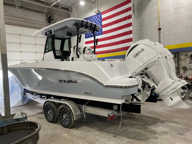 The Image of 2025 Stingray 253CC boat with Yamaha engine in a garage, American flag backdrop. - 1