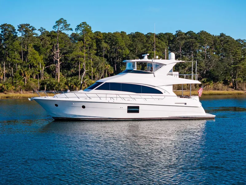 Slide: The Image of 2016 Hatteras M60 yacht cruising on a serene lake with forested background. - 1