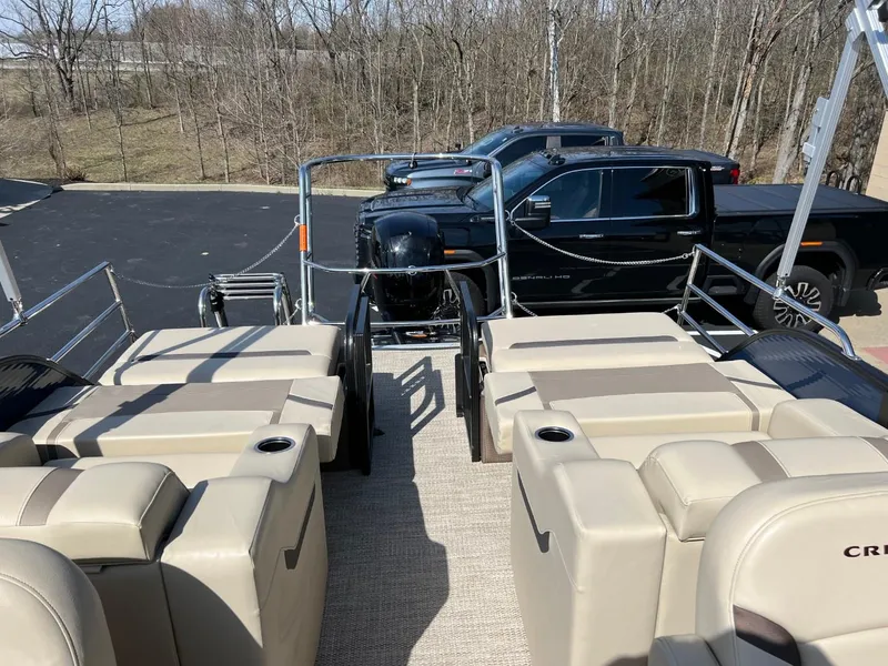 Slide: The Image of 2024 Crest Classic LX 220 pontoon boat with beige seating, parked near black trucks. - 11