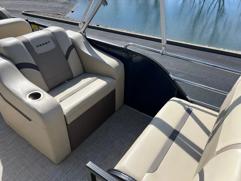 Slide: The Image of 2024 Crest Classic LX 220 boat interior with beige seating and cup holder by the water. - 12