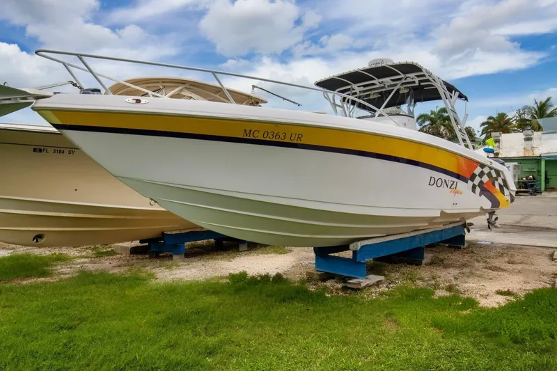 The Image of 2005 Donzi 35 ZF Cuddy boat on display, white hull with yellow stripe, parked on grass. - 1