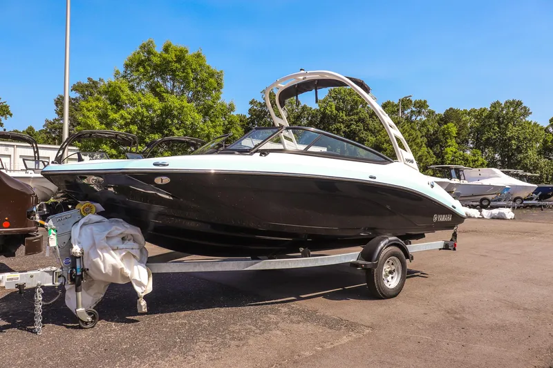 The Image of 2025 Yamaha Boats 195S on trailer, parked outdoors, surrounded by trees and other boats. - 1