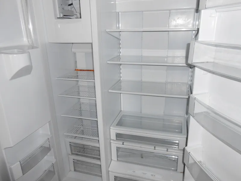 Slide: The Image of Empty refrigerator interior on a 1999 Horizon houseboat, featuring multiple shelves and compartments. - 14