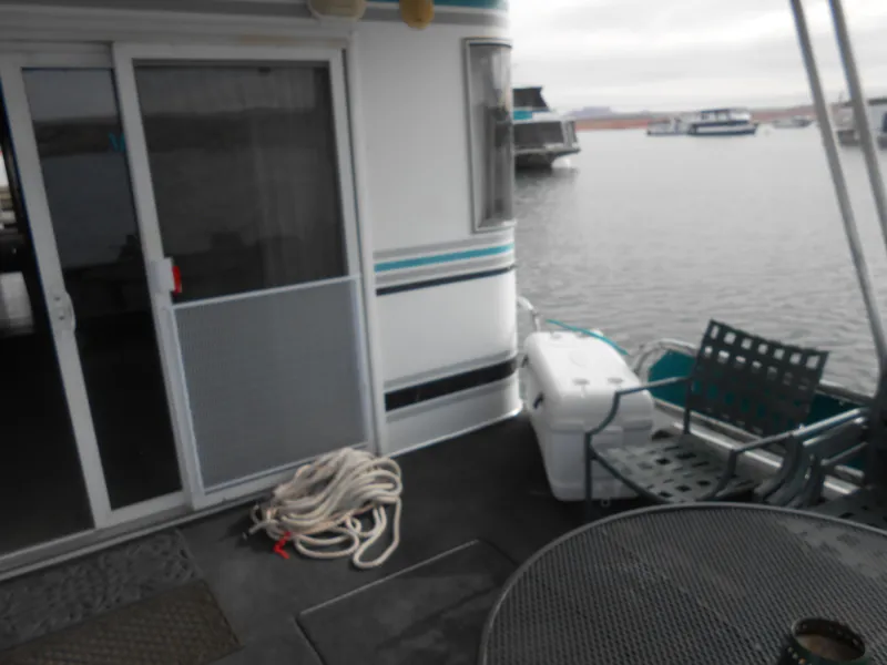 Slide: The Image of 1999 Horizon houseboat deck with chairs, table, and coiled rope by the water. - 6