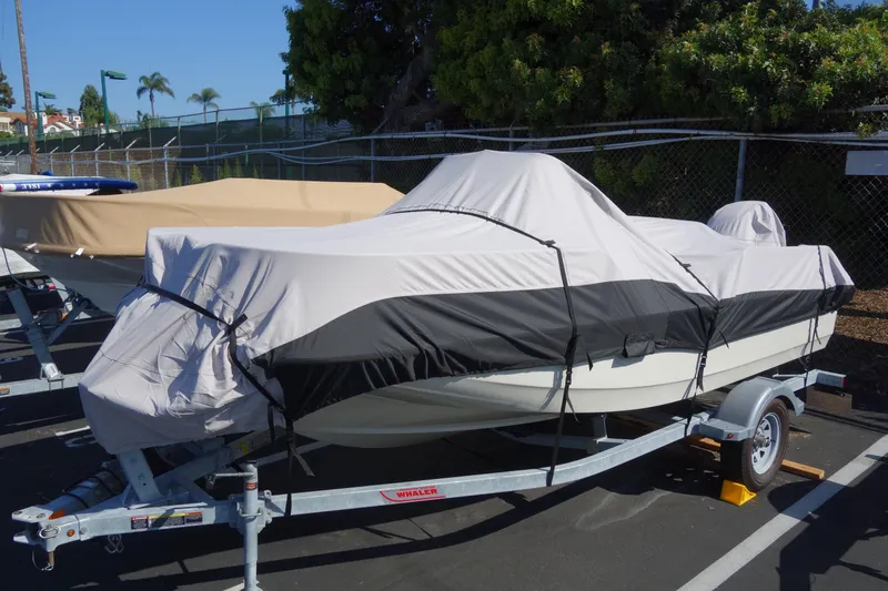 Slide: The Image of 2023 Boston Whaler 150 Montauk boat covered on a trailer in a parking lot. - 2