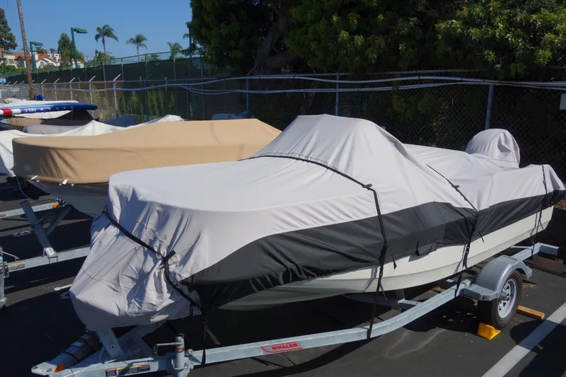 Slide: The Image of 2023 Boston Whaler 150 Montauk boat covered and parked on a trailer. - 3