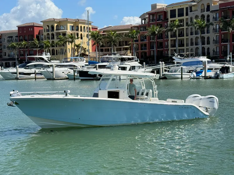 Slide: The Image of 2023 Cobia 350 Center Console boat docked in a marina with luxury buildings. - 0