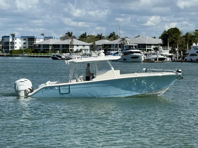 Slide: The Image of 2023 Cobia 350 Center Console boat on water near marina, under partly cloudy sky. - 6