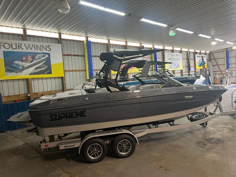 Slide: The Image of 2024 Supreme S220 boat in showroom, on trailer, with banners in background. - 2