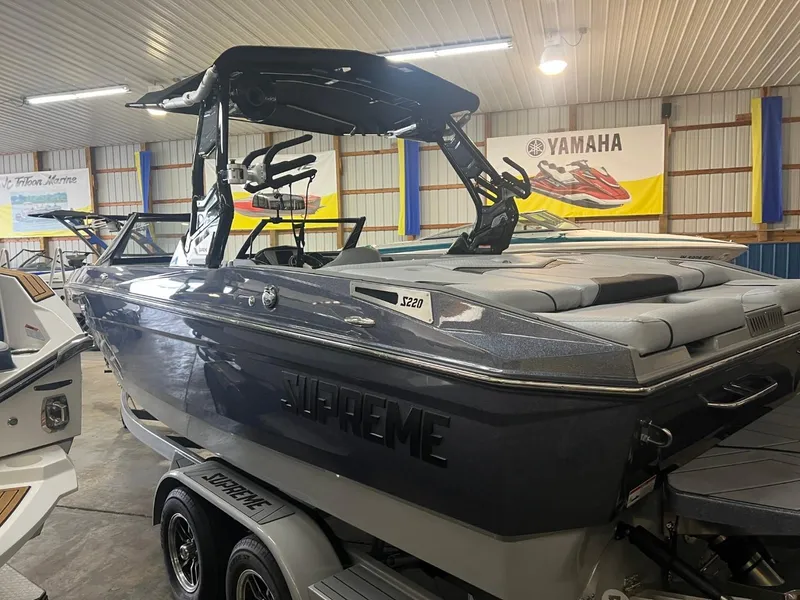 Slide: The Image of 2024 Supreme S220 boat in showroom, sleek design, dual-axle trailer. - 33