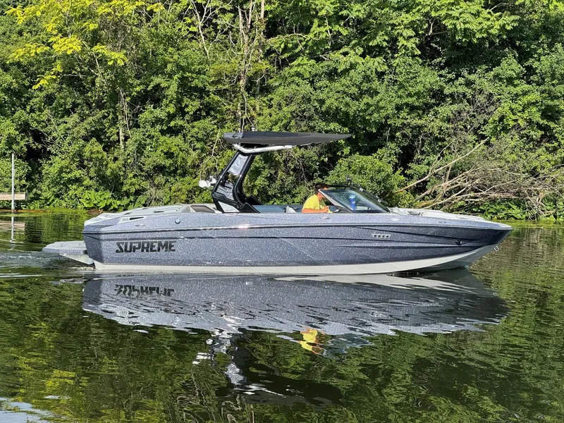 Slide: The Image of 2024 Supreme S220 boat cruising on a calm lake with lush green trees in the background. - 4